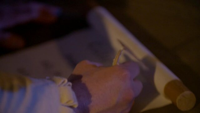 Closeup of hand wiring on manuscript, lit by candlelight, renaissance themed