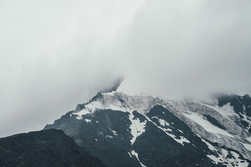 Minimalist monochrome atmospheric mountains landscape with big snowy mountain top in low clouds. Awesome minimal scenery with glacier on rocks. Black white high mountain pinnacle with snow in clouds.
