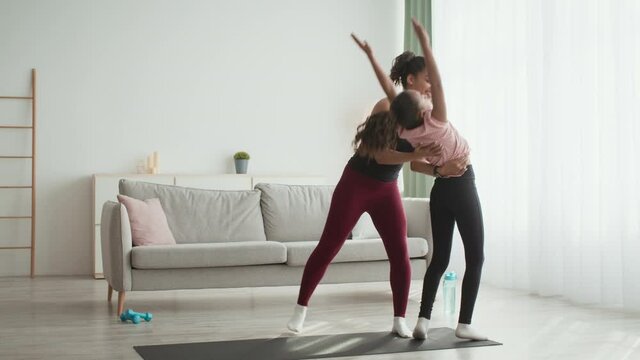 Acrobatic practice. Flexible african american girl practicing coup exercise with help of her mother at home