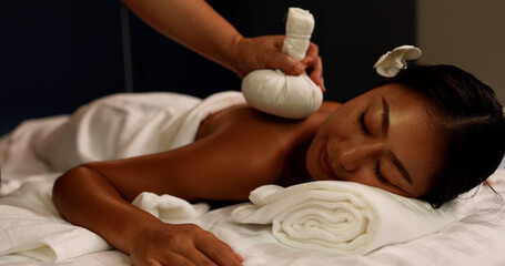 Obraz na płótnie Canvas Young Asian woman receiving back massage with Thai herbal compress ball at spa salon by professional masseuse, Spa treatment and thai massage concept