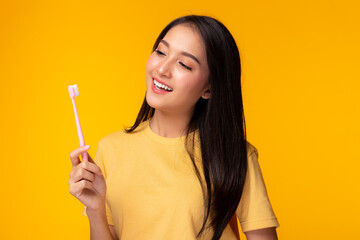Happy woman take care tooth and holding toothbrush Young lady brushing her teeth Beautiful asian girl has beautiful tooth, white teeth nice tooth alignment Yellow background, copy space Dental care