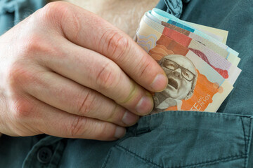 the man takes a bundle of columbian pesos from his shirt pocket