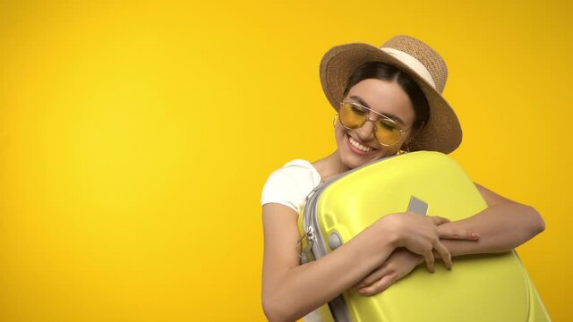 Smiling traveler hugging suitcase isolated on yellow