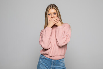 Portrait of a young woman covering her mouth with palm and looking away over gray background