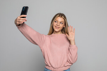 Smiling young woman making selfie photo on smartphone over gray background