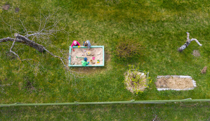 Aerial top-down view on the spring green backyard garden with the sandbox and kids playing
