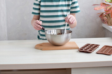 Step by step the boy prepares handmade chocolate at home. Stir the liquid chocolate with a spatula on a light table.