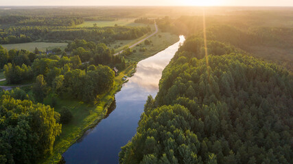 Aerial view along natural river toward sunny morning horizon and wilderness of the national park on the right side and rural landscape on the left