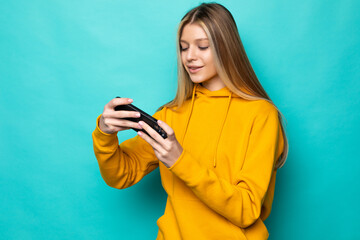 Young woman play game with mobile phone posing isolated on blue turquoise background