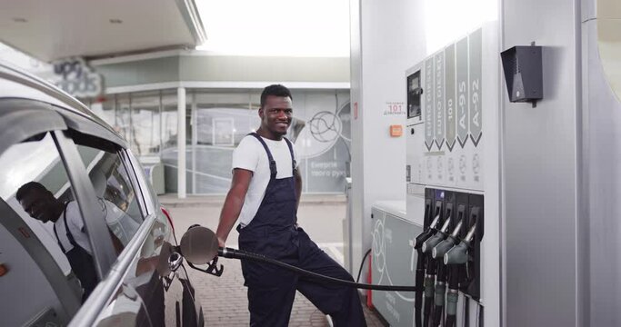 Young handsome African male worker at gas station refueling client's car with petrol. Translational: ENERGY MOVEMENT