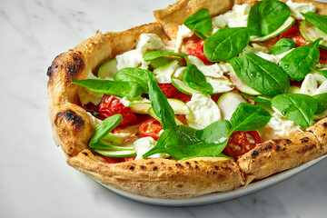 Delicious pizza with zucchini, burrata, sun-dried tomatoes, and spinach on a white plate on a white marble background