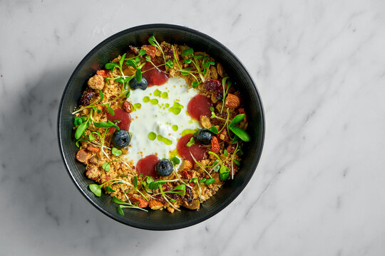 Healthy breakfast bowl of granola with dried fruits, berries, nuts, microgrin and yogurt on a light marble background