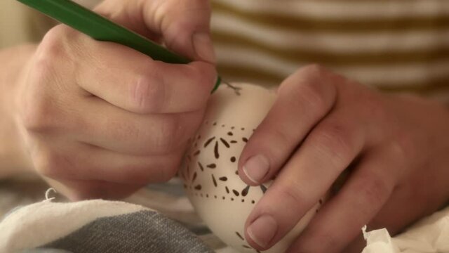 Hand carefully decorates ornate pattern on Easter madeira egg, close-up