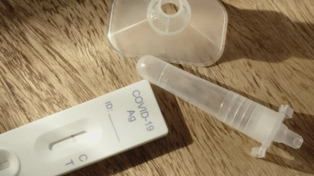 COVID-19 antigen test kit dropped onto wood table, slow zoom