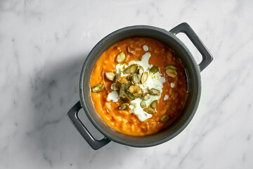 Pumpkin porridge with pumpkin seeds in green pot on light marble background