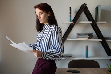 A young European girl, teacher or consultant, stands at a table in the office and gives a talk. Remote work or science concept.
