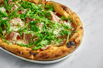 Delicious pizza with prosciutto, tomato sauce, parmesan and arugula on a white plate on a white marble background