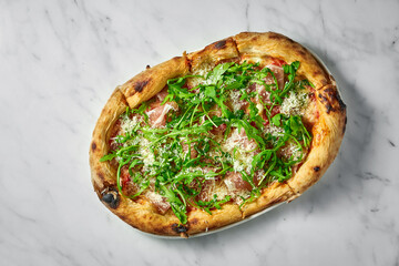 Delicious pizza with prosciutto, tomato sauce, parmesan and arugula on a white plate on a white marble background