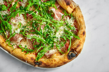 Delicious pizza with prosciutto, tomato sauce, parmesan and arugula on a white plate on a white marble background