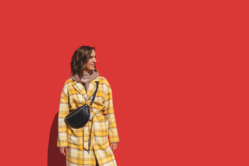 Beautiful Caucasian girl in a yellow coat on a bright red background in sunbeams. Autumn city outfit