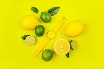 Bright summer citrus flatlay with watches, lemons and limes isolated on yellow background.