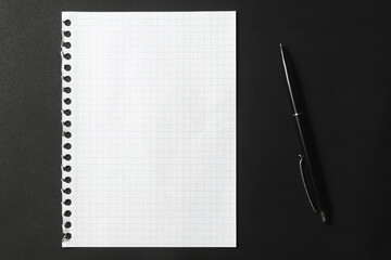 A white piece of paper from a notebook and a black pen on a dark background.