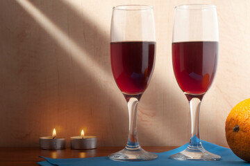 Still life with two glasses of wine on a blue napkin, an orange and two burning candles.