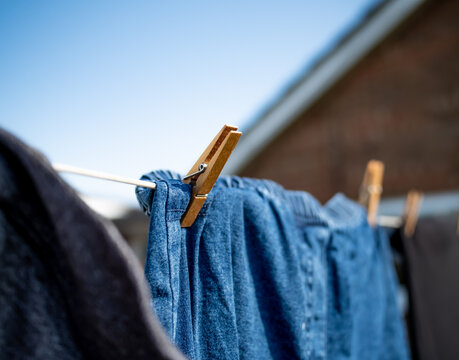 Close And Selective Focus On A Wooden Clothes Peg Keeping A Pair Of Blue Denim Pants Or Jeans On A Washing Line With Intentional Shallow Depth Of Fiels And Bokeh