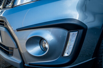 The front fog light and LED driving light on the front of a grey Suzuki motor vehicle with intentional shallow depth of field and bokeh