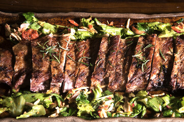 Delicious grilled ribs seasoned with a spicy sauce and served with chopped fresh vegetables on an old rustic wooden board in a country kitchen. View from the top.