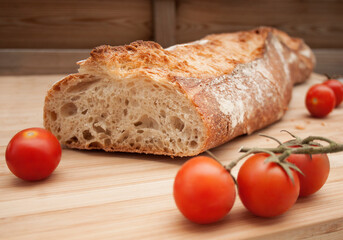 Fresh colorful cherry tomatoes on wooden table. Freshly baked bread and metallic knife on background.