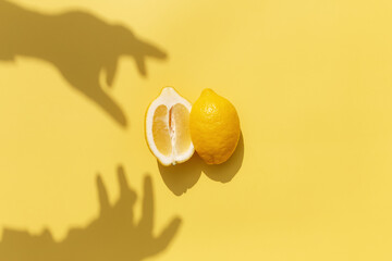 Two halved cuts of lemon with shadow from hand on yellow background