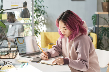 Young Chinese woman sitting at the table and writing she doing her work during study