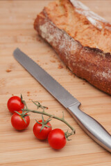 Tomatoes cherry freshly baked bread and knife on the wooden table. Bread crumbles on the table.
