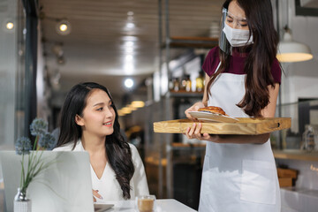 Asian waitress with face protective mask and face shield serving coffee and bread in coffee shop