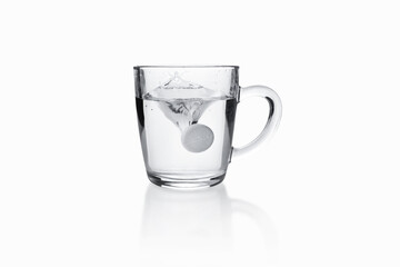 Soluble tablet sinking with splash to transparent glass mug on white background.