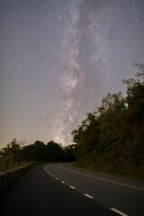 Naklejka premium The Milky Way galaxy rising over a curving mountain road
