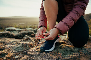 Close up caucasian female hiker tying shoe lace while walking through luscious mountain