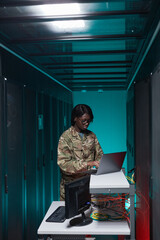 Vertical portrait of young African-American woman wearing military uniform using computer while...