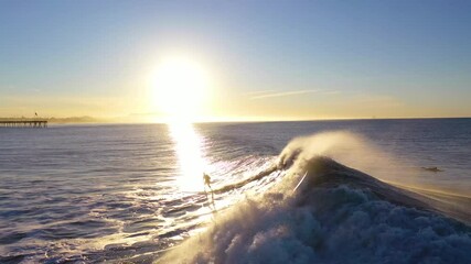Aerial of surfer surfing riding large ocean waves with surf breaking off the coast of Ventura, California.