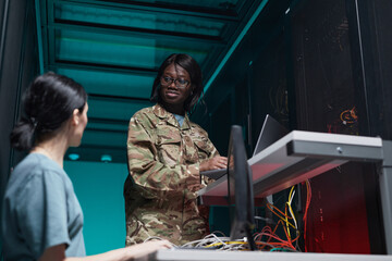 Fototapeta na wymiar Low angle portrait of young African-American woman wearing military uniform using computer while setting up network in server room