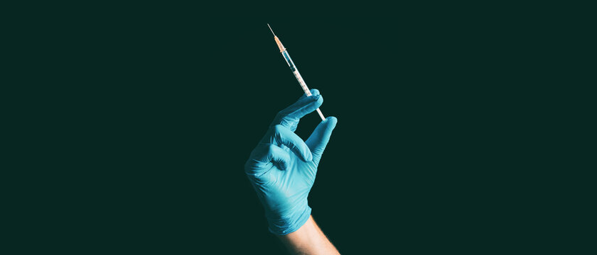 Coronavirus Vaccine Syringe Held By Doctor Or Nurse In Blue Medical Ppe Glove Against Black Background Banner.