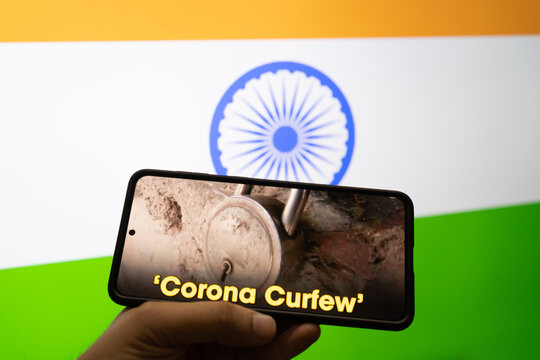 man holding a mobile phone with news on corona curfew and the india tri color flag in the background showing the self lockdown during the second stage of the pandemic