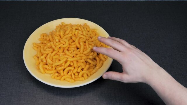 A hand reaches for unhealthy snacks on a yellow plate. A child's hand comes in and slaps the adult's hand so he pulls it away from the snack. Do not choose cheese snack!