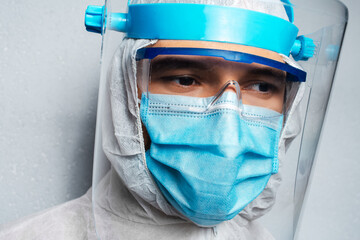 Obraz na płótnie Canvas Studio portrait of young doctor man wearing PPE suit against coronavirus and covid-19, on background of grey wall.