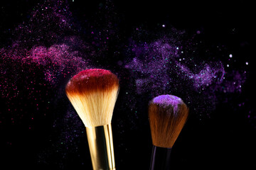 Cosmetics brushes and explosion pink purple makeup powder. Makeup brush with colorful powder mixed in explosion on black background close up. Beauty product eye shadows or blusher concept