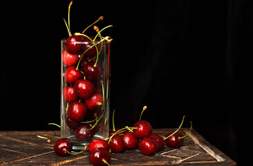 A glass with ripe cherries stands on a dark cutting board