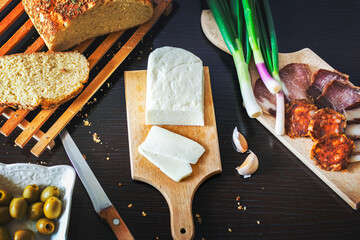 Haloumi cheese with freshly baked bread, green onions, smoked ham and sausage, olives on a dark wooden dining table.