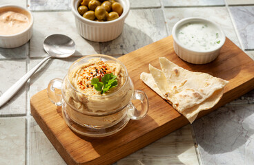 Glass jar of hummus, traditional Jewish, Arabian, Middle Eastern food from chick-peas with deeps and with pita flatbread on ceramic tile background. Close up, selective focus