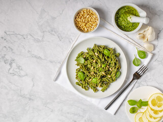 Green fussili pasta made of mungo beans with vegan homemade basil pesto and herbs. Italian pasta. Italian food. Home made food. Concept for a tasty and healthy meal. Gray stone background. Top view.